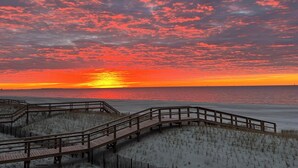 Un muelle de madera que conduce a una playa con un atardecer de fondo.