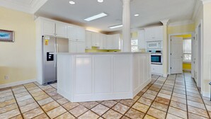 Una cocina amplia con armarios blancos, una isla central y piso de baldosas.