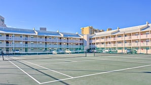 A multi-story hotel with a tennis court in front. - Coastal condo with water views, shared pool, and tennis court (Orange Beach)