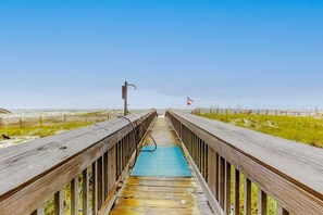 A wooden boardwalk leading to a beach with a blue mat in the center. - Beachfront condo with private balcony, shared pool, and hot tub (Orange Beach)