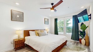 A bedroom with a bed, nightstands, a ceiling fan, a window with curtains, and a wall-mounted TV. - Cozy townhome located near The Wharf concert and event venue! (Orange Beach)