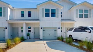 A row of white two-story houses with attached garages, a driveway, and a parked SUV. - Cozy townhome located near The Wharf concert and event venue! (Orange Beach)