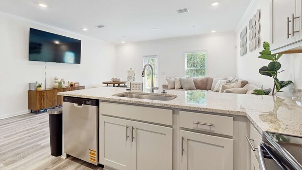 A modern kitchen with a dishwasher, a large island with a sink, and a flat-screen TV mounted on the wall. - Cozy townhome located near The Wharf concert and event venue! (Orange Beach)