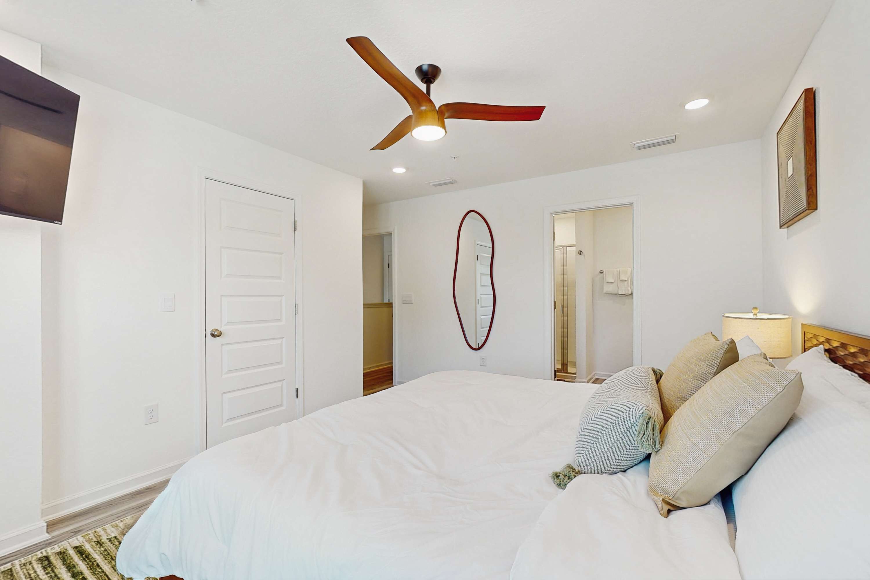 A bedroom with a bed, a ceiling fan, a mirror, and a nightstand with a lamp.