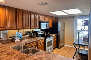 A kitchen with wooden cabinets, a stainless steel sink, a microwave, a stove, and a refrigerator. - Beachfront condo with pool, private balcony, & washer and dryer! (Orange Beach)
