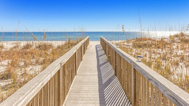Ein hölzerner Steg führt zu einem Strand unter blauem Himmel.