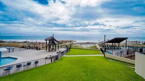 A rooftop pool area with a view of the beach, a grassy lawn, and a wooden deck. - Beautiful beachfront condo with hot tub, pool, sauna, tennis, gym, & balcony (Orange Beach)