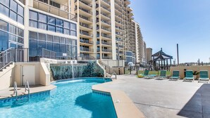 A swimming pool with steps leading into it, a gazebo, and lounge chairs on a sunny day. - Beautiful beachfront condo with hot tub, pool, sauna, tennis, gym, & balcony (Orange Beach)