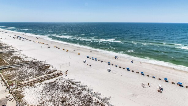 A beach with a long stretch of sand, a few umbrellas, and a clear view of the ocean. - Beautiful beachfront condo with hot tub, pool, sauna, tennis, gym, & balcony (Orange Beach)