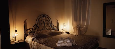 Una camera da letto poco illuminata, con un letto, due abat-jour, uno specchio e una finestra con tenda.