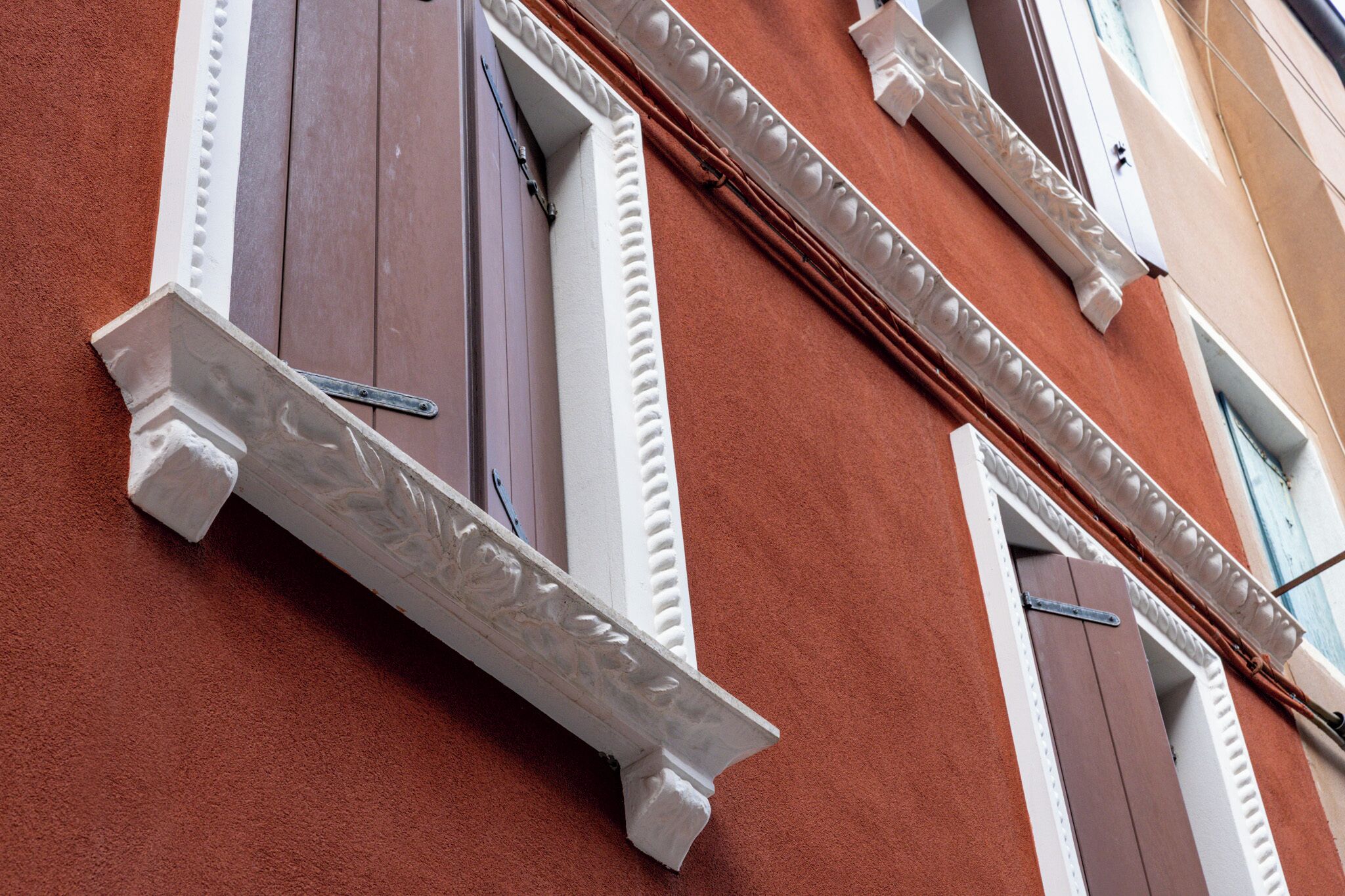 Fachada de un edificio con paredes de estuco rojo, marcos de ventanas blancos y molduras decorativas.