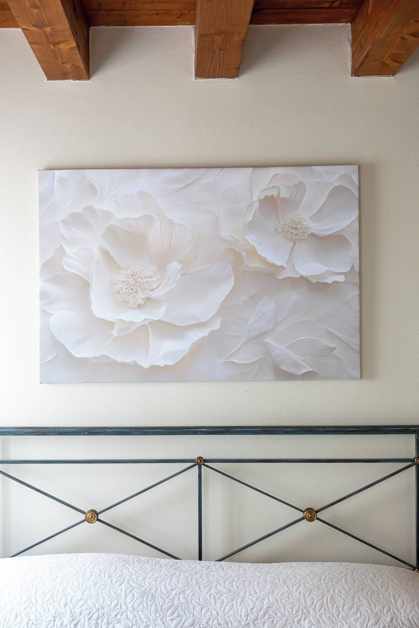A bed with a metal headboard, a white wall, and a large floral painting above it.
