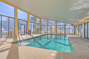 Una piscina interior con paredes de vidrio transparente, suelo de baldosas y una silla para socorrista.