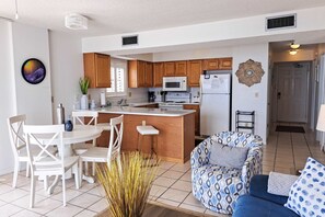 Una cocina moderna con armarios de madera, una isla central y un comedor con sillas blancas.
