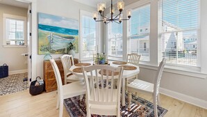 A dining area with a white table, chairs, a chandelier, and a painting of a beach scene.
