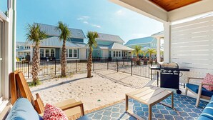 A covered outdoor area with a patio, seating, a grill, and a view of houses in the background.