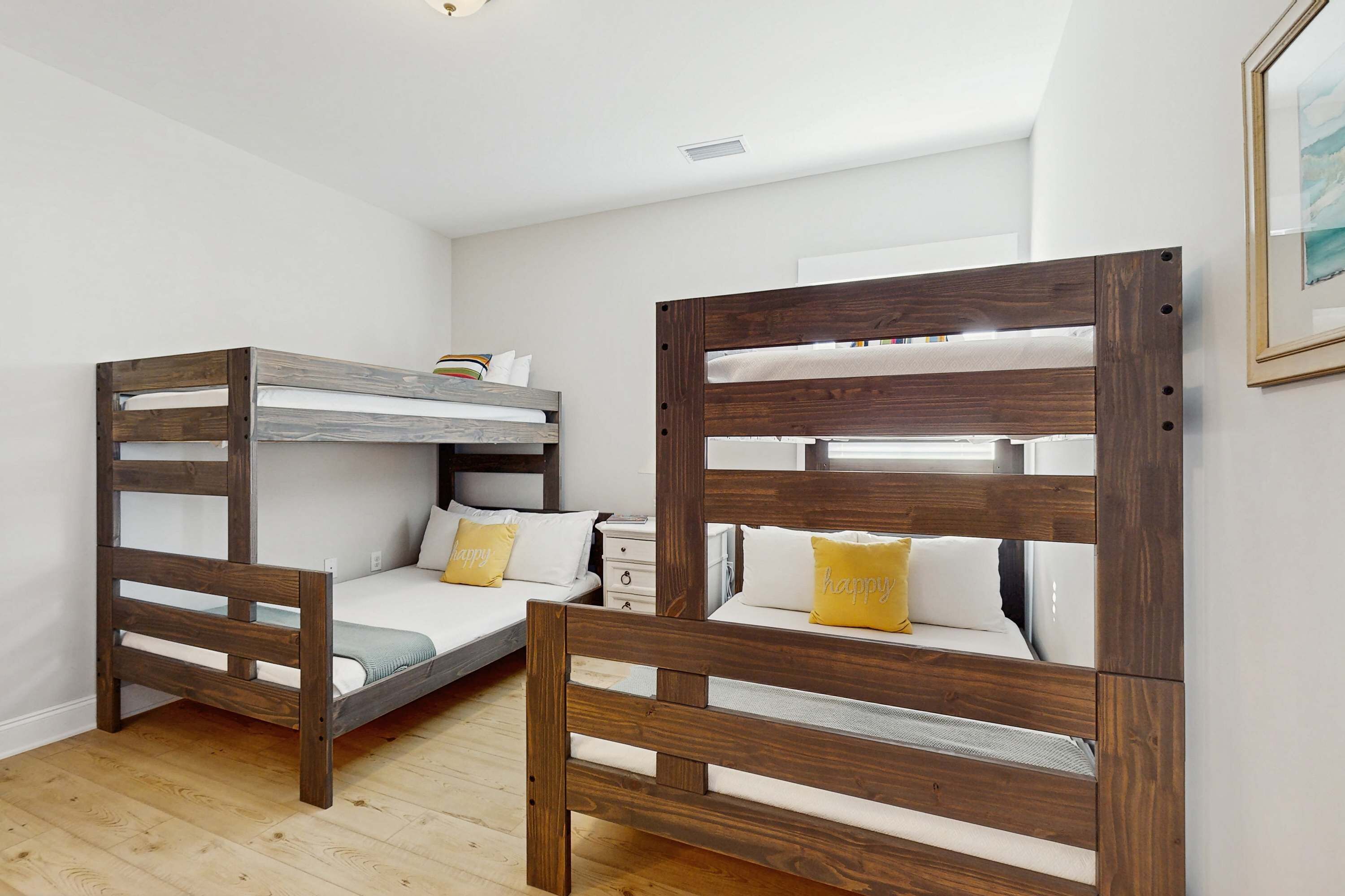 Ein Zimmer mit zwei Etagenbetten, einer kleinen weißen Kommode und einem gerahmten Bild an der Wand.