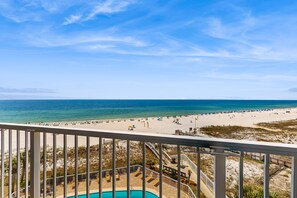 Blick auf einen Strand von einem Balkon mit Pool und Liegestühlen.