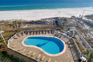 Ein Pool mit gewölbter Kante, umgeben von einer Liegefläche mit Liegestühlen, in Strandnähe.