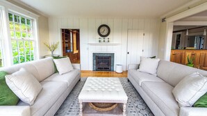 A living room with two sofas, a coffee table, a fireplace, and a large wall clock. - 3-bedroom house in Stowe with stunning panoramic views and ~11 acres to explore. (Stowe)