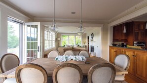 A dining room with a large wooden table, six upholstered chairs, and hanging pendant lights. - 3-bedroom house in Stowe with stunning panoramic views and ~11 acres to explore. (Stowe)