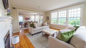 A spacious living room with a fireplace, a large window, and a dining area in the background. - 3-bedroom house in Stowe with stunning panoramic views and ~11 acres to explore. (Stowe)