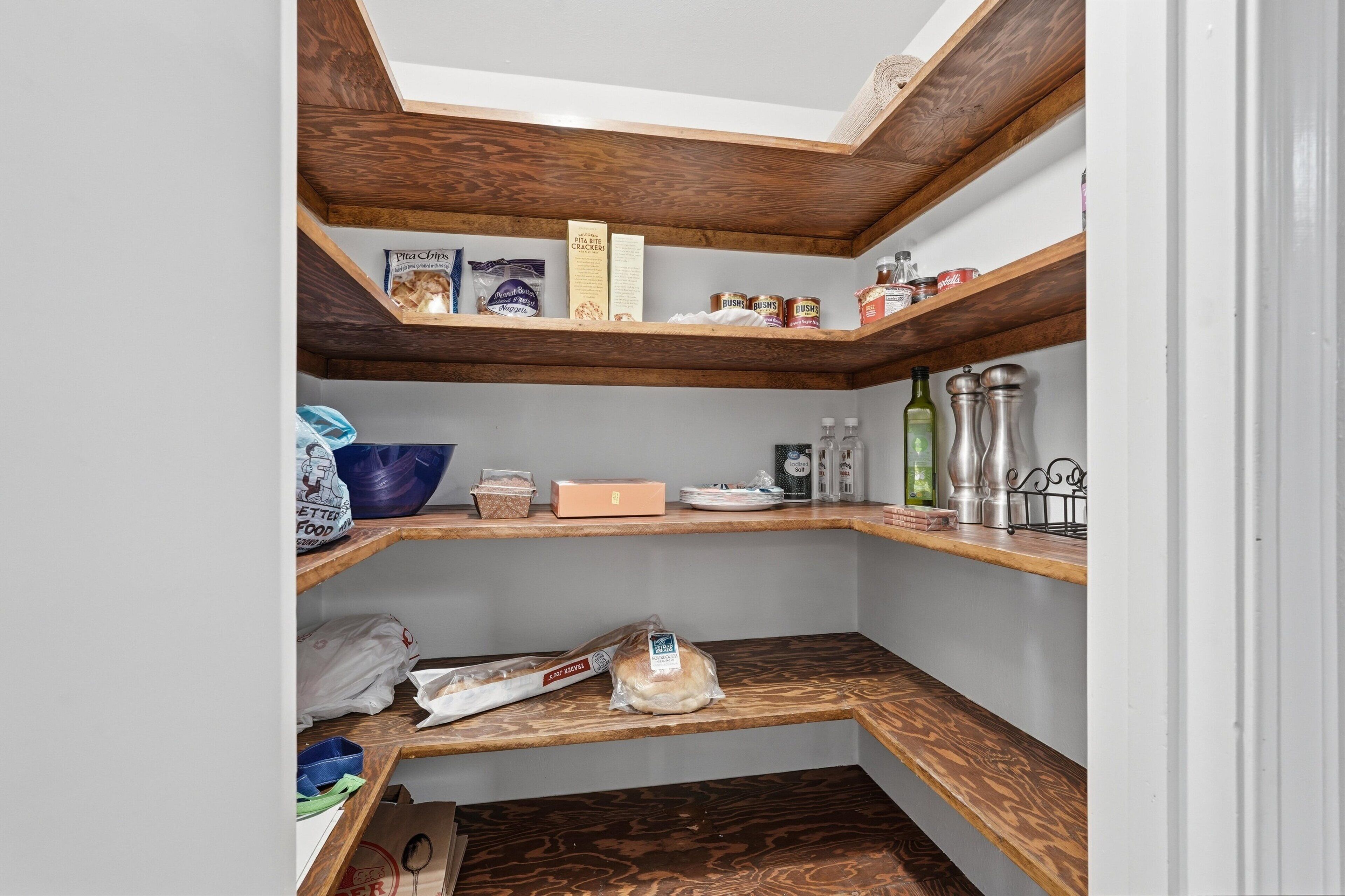 Una cocina con estantes de madera, una bolsa de pan y diversos alimentos.