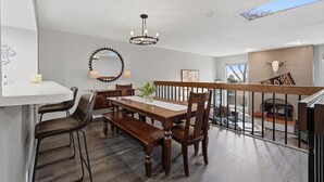 Un comedor con mesa de madera, sillas, un banco, una araña y una chimenea.