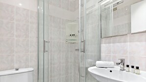 A modern bathroom with a glass-enclosed shower, a white sink with toiletries, and a toilet. - Studio Raffine Quartier La Muette (Paris)