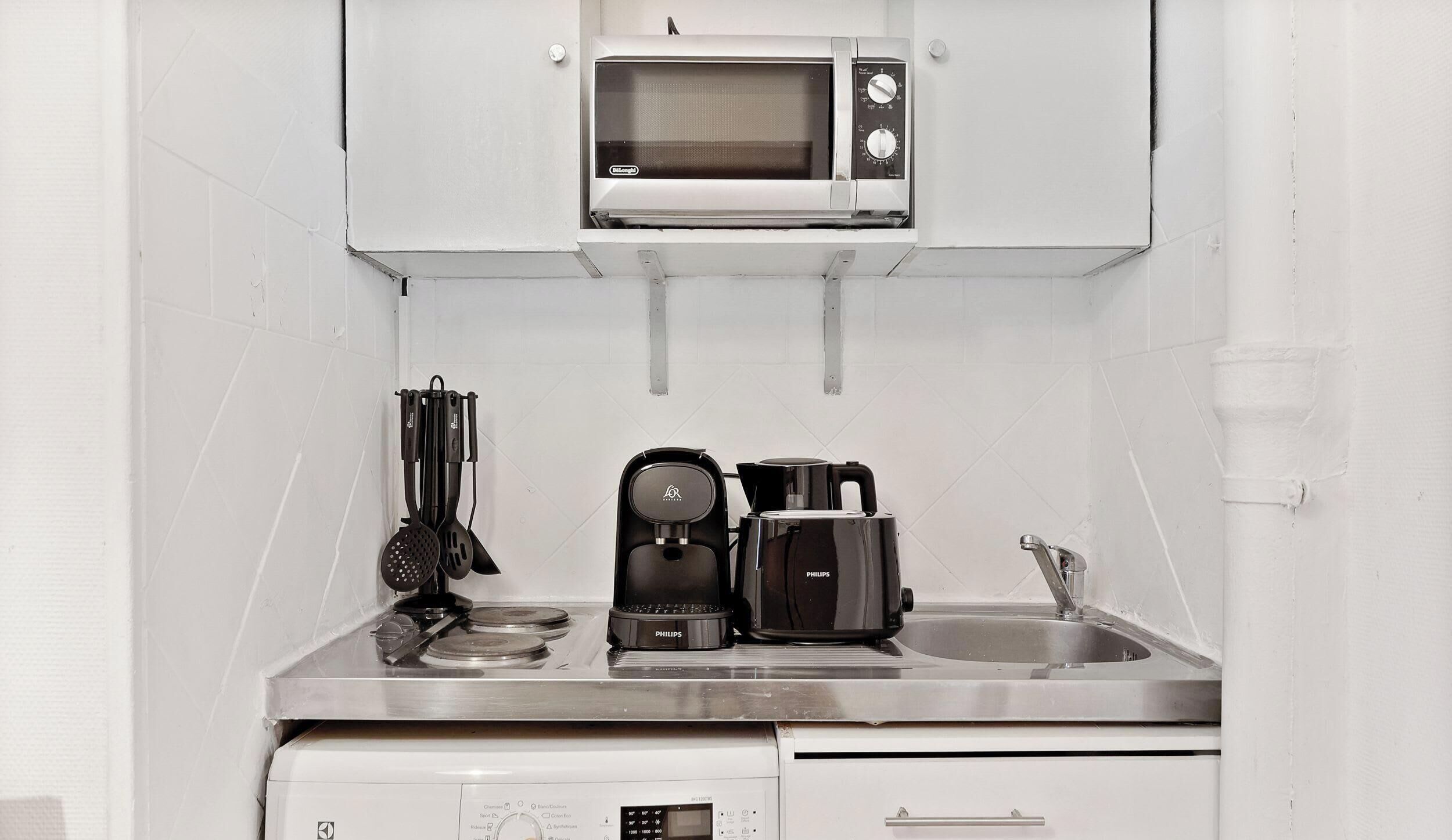 Eine kleine Küchenzeile mit Mikrowelle, Kaffeemaschine und Spüle.
