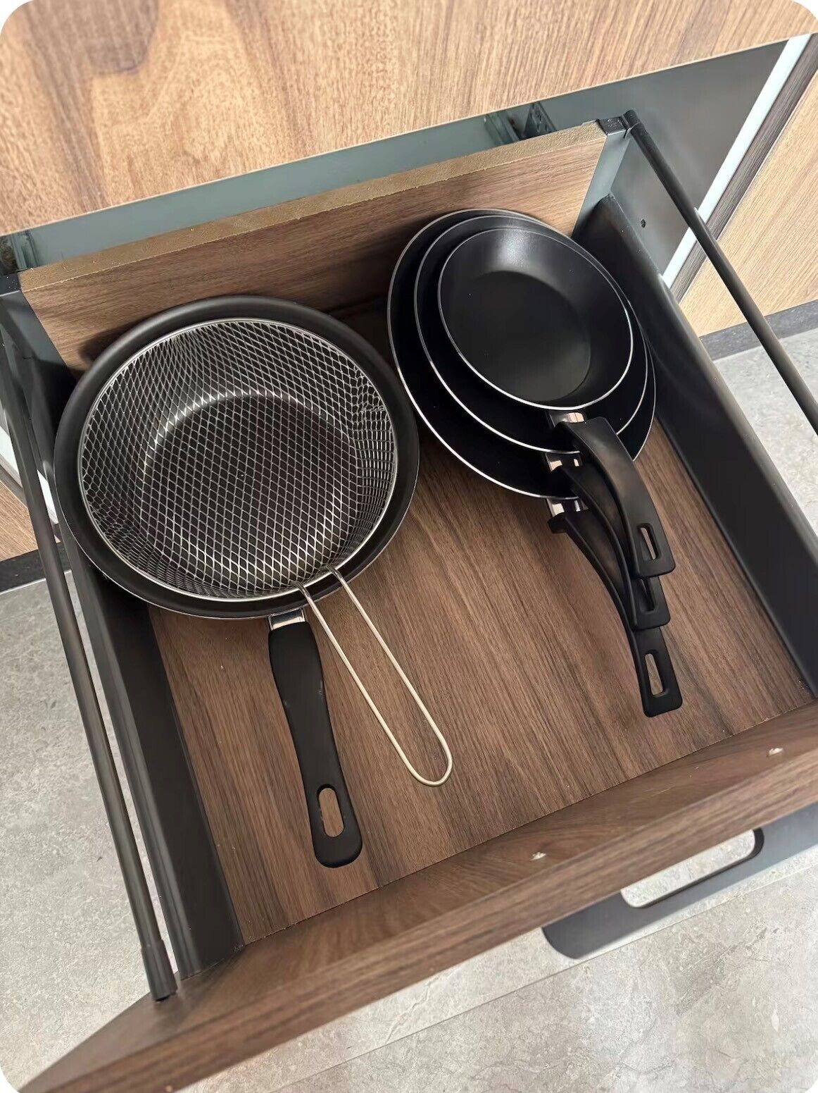 Een houten lade met twee keukenaccessoires: een vergiet en een anti-aanbakpan.