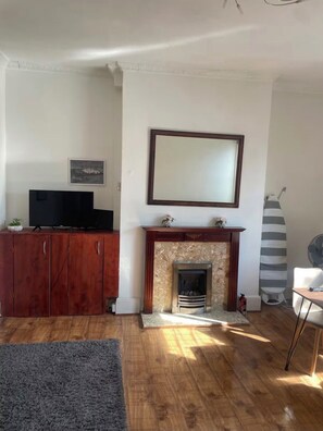 Ein Wohnzimmer mit Kamin, Holzboden, Fernseher auf einem Schrank und einem großen Spiegel an der Wand.