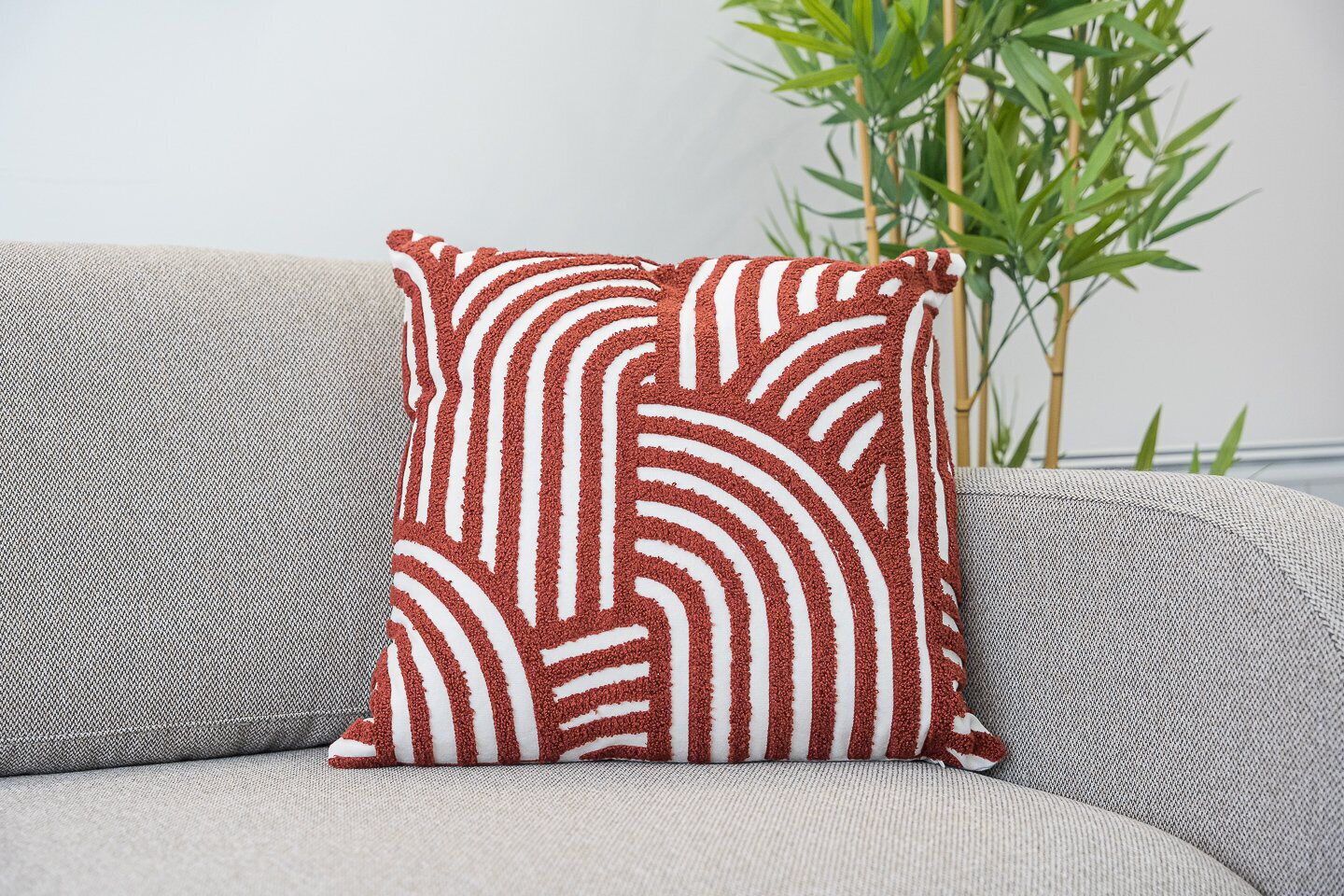 A square cushion with a red and white striped pattern on a grey sofa.