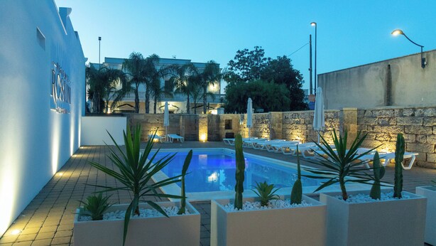 A swimming pool with lounge chairs and planters, surrounded by a stone wall and palm trees. - Residence Rossini Suites & Poll (Alliste)