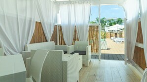 A room with wicker furniture, a wooden floor, and a view of an outdoor area with umbrellas. - Residence Rossini Suites & Poll (Alliste)