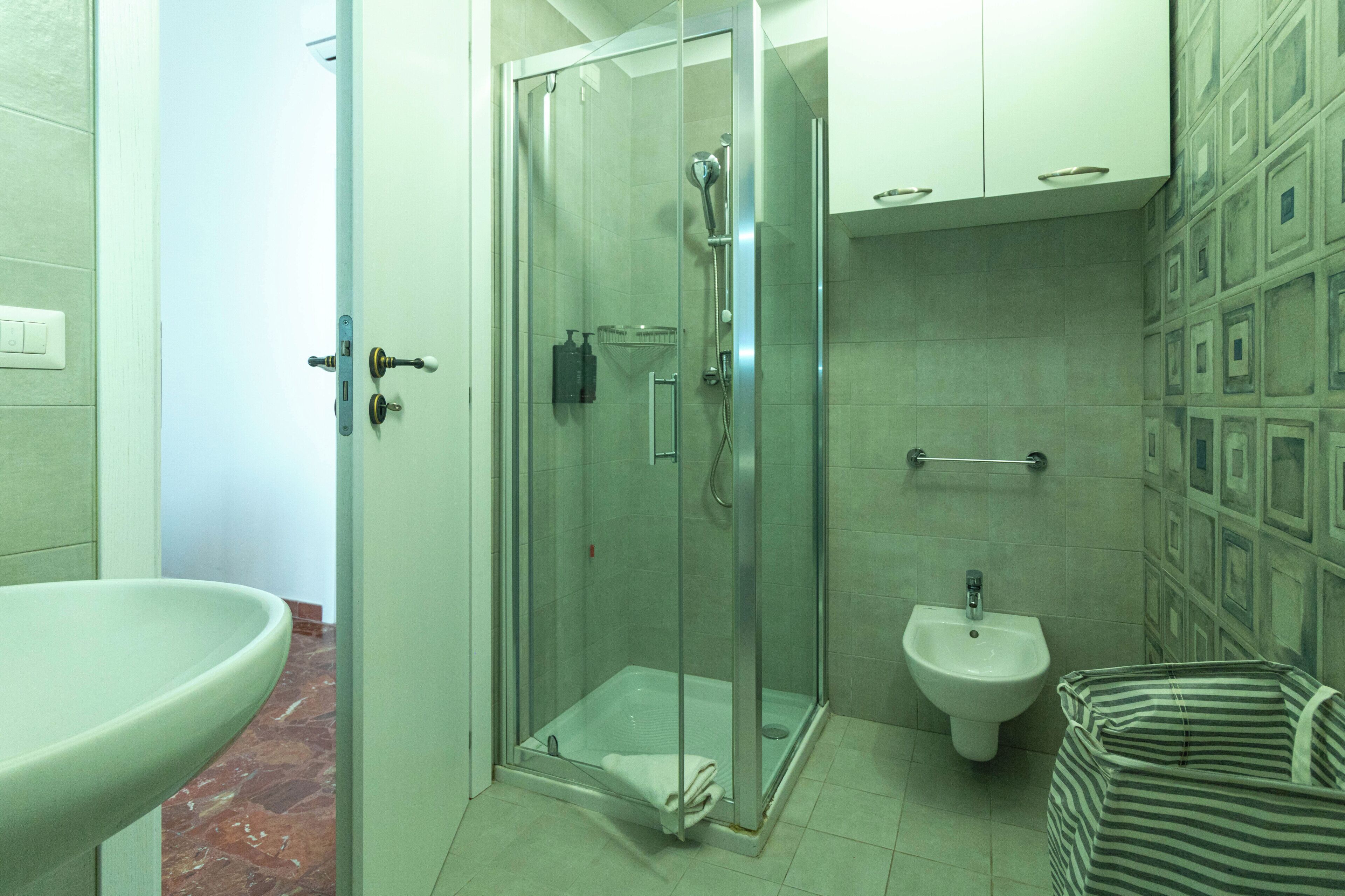 A bathroom with a glass-enclosed shower, a pedestal sink, a bidet, and a striped bag.