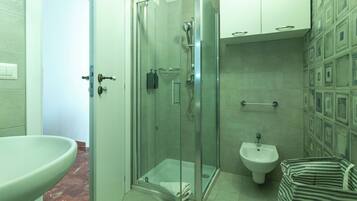 A bathroom with a glass-enclosed shower, a pedestal sink, a bidet, and a striped bag.