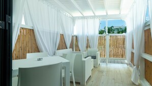 A covered patio area with white furniture, bamboo walls, and a view of the outdoors. - Residence Rossini Suites & Poll (Alliste)