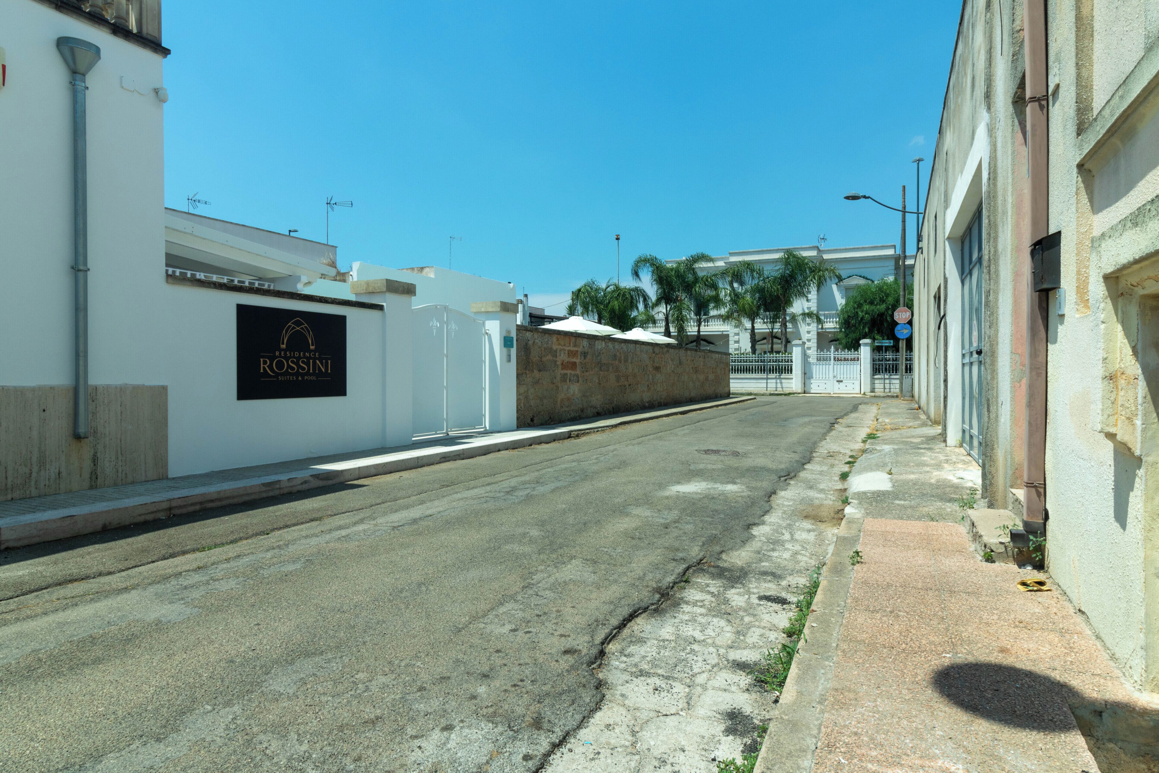 Une vue de rue avec un bâtiment portant l’inscription « ROSSINI » sur la gauche, un trottoir et un ciel bleu dégagé.