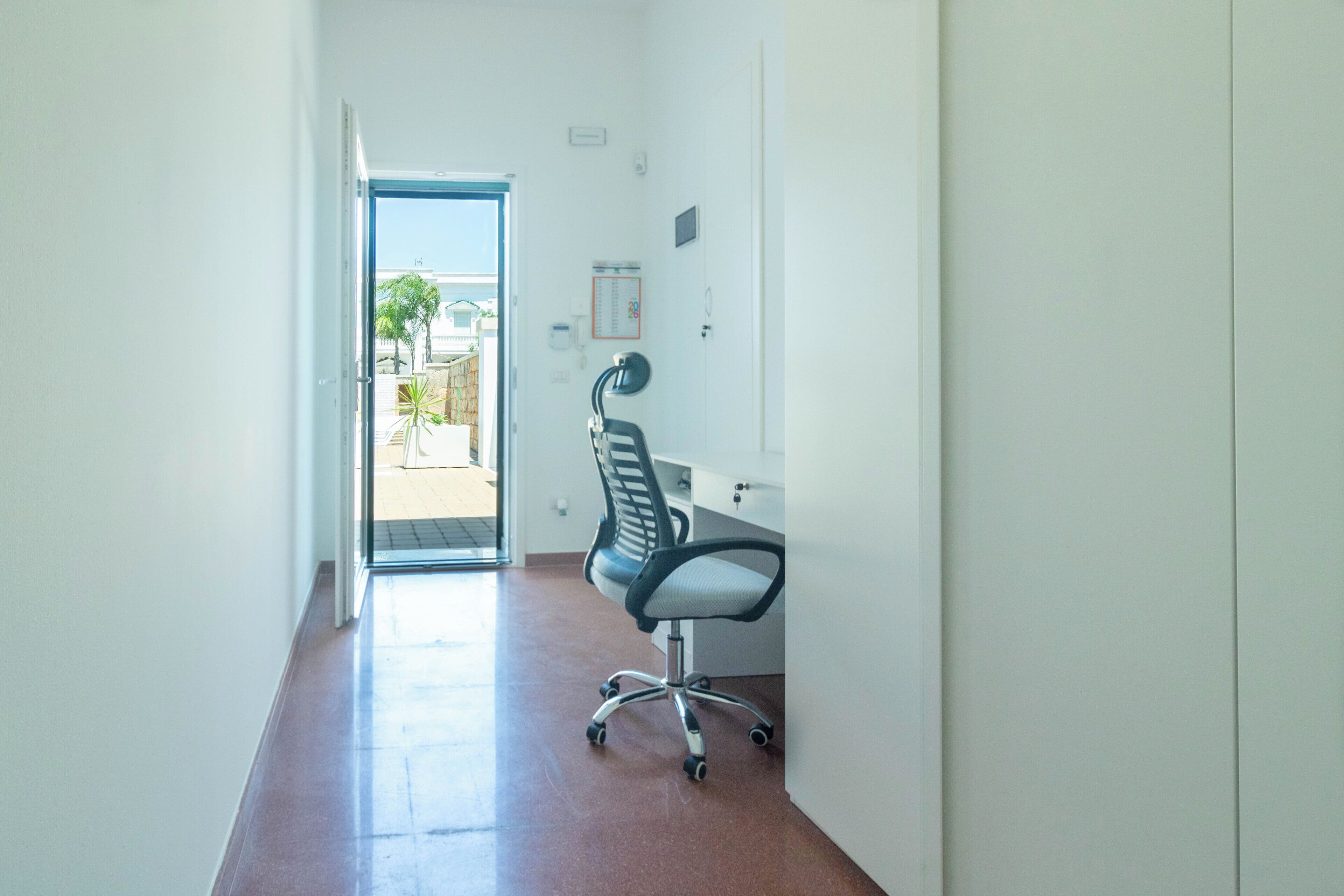 Un couloir menant à une porte, un bureau avec une chaise et une petite fenêtre.