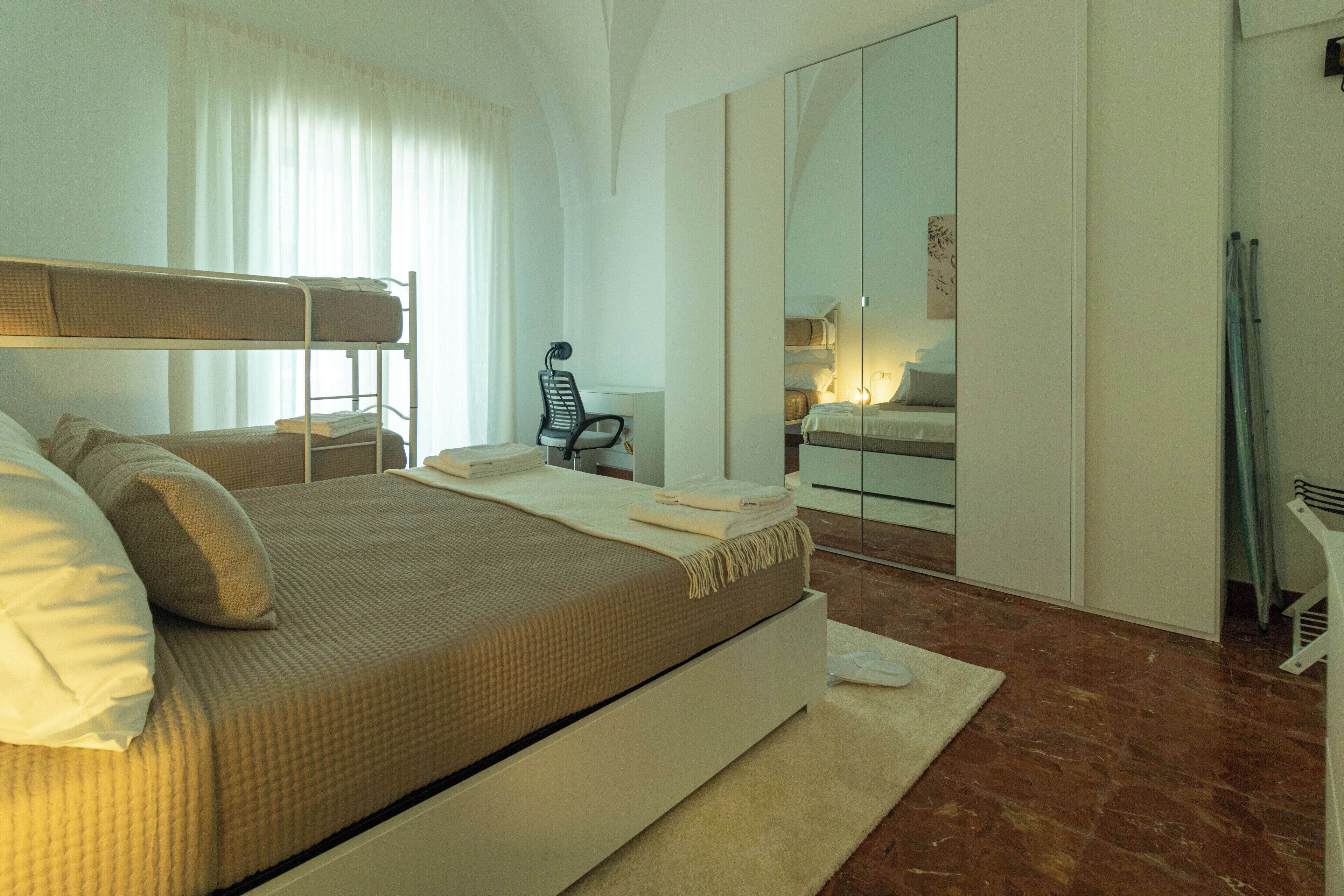 Una habitación de hotel moderna con una litera, un escritorio, una silla, un armario y un espejo.