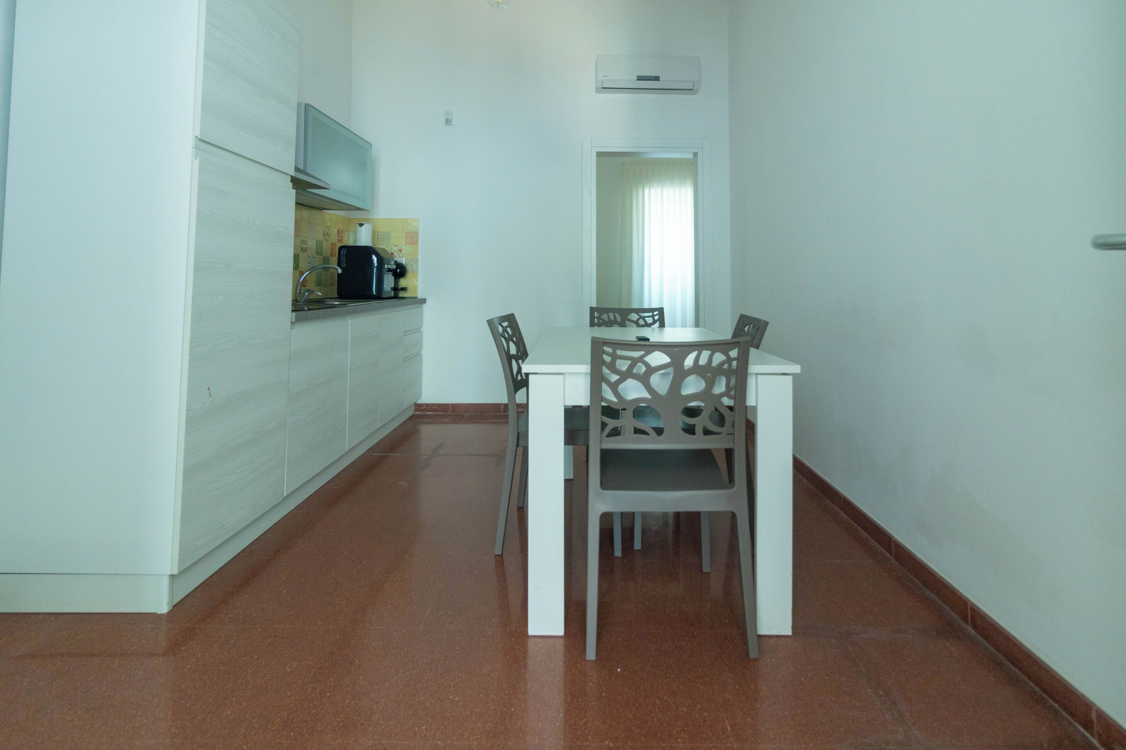 Habitació petita i neta amb cuineta, taula de dinar i cadires, i un mirall a la paret.