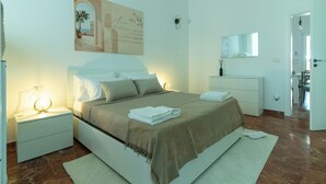 A bedroom with a bed, nightstands, a bedside table, a mirror, and a door leading to another room. - Residence Rossini Suites & Poll (Alliste)