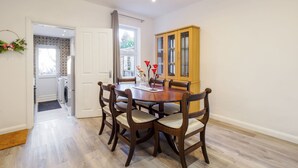 A dining area with a wooden table and chairs, a cabinet, and a view of a laundry room through an open door. - Host & Stay | Roach Street (Rochester)