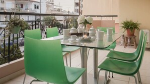 Un balcon avec une table en verre dressée pour le thé, des chaises vertes et des plantes en pot.