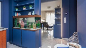 Un hall d’hôtel moderne aux couleurs dominantes bleues, avec un comptoir d’accueil, un espace salon et un aquarium décoratif.