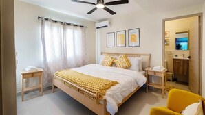 Ein Schlafzimmer mit einem Bett, einem Deckenventilator, einem Nachttisch, einem Sessel und einem durch eine offene Tür einsehbaren Badezimmer.