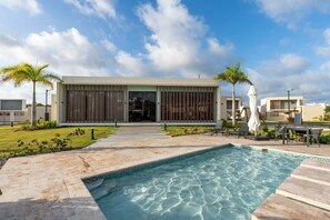 A modern building with a swimming pool, outdoor seating, and palm trees. - Atabey Luxury Paradise (Punta Cana)