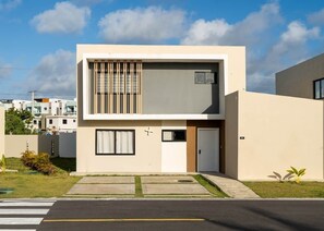 Une maison moderne à deux étages, dotée d’un toit plat, d’une porte d’entrée et d’un petit jardin.