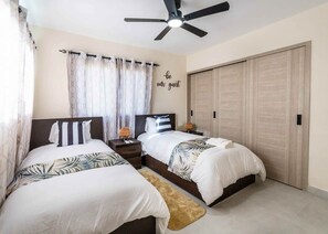 Une chambre d’hôtel avec deux lits, un ventilateur de plafond, une armoire et un mur orné d’une pancarte indiquant « soyez les bienvenus ».